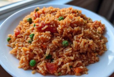 Close-up of a serving of fluffy spanish rice mixed with bright green peas and chunks of tomato on a white plate.