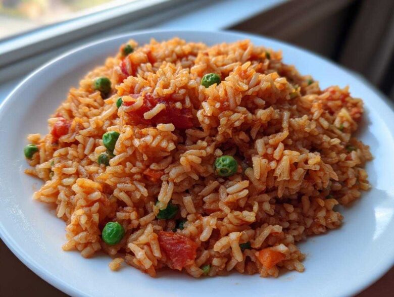 Close-up of a serving of fluffy spanish rice mixed with bright green peas and chunks of tomato on a white plate.