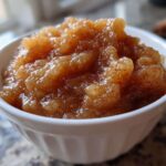 Close-up of chunky, homemade applesauce seasoned with cinnamon served in a small white bowl.