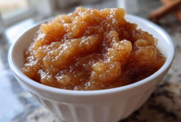 Close-up of chunky, homemade applesauce seasoned with cinnamon served in a small white bowl.