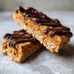 Two stacked homemade protein bars made with oats and peanut butter, topped with a dark chocolate drizzle.