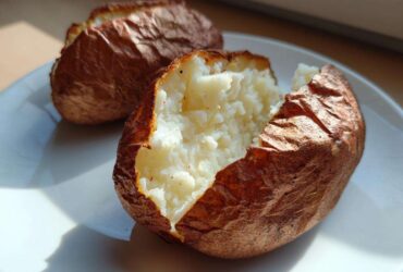 Close-up of a perfectly cooked air fryer baked potato, split open revealing fluffy white interior.