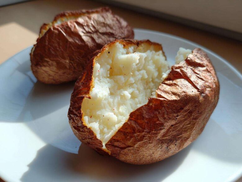 Close-up of a perfectly cooked air fryer baked potato, split open revealing fluffy white interior.