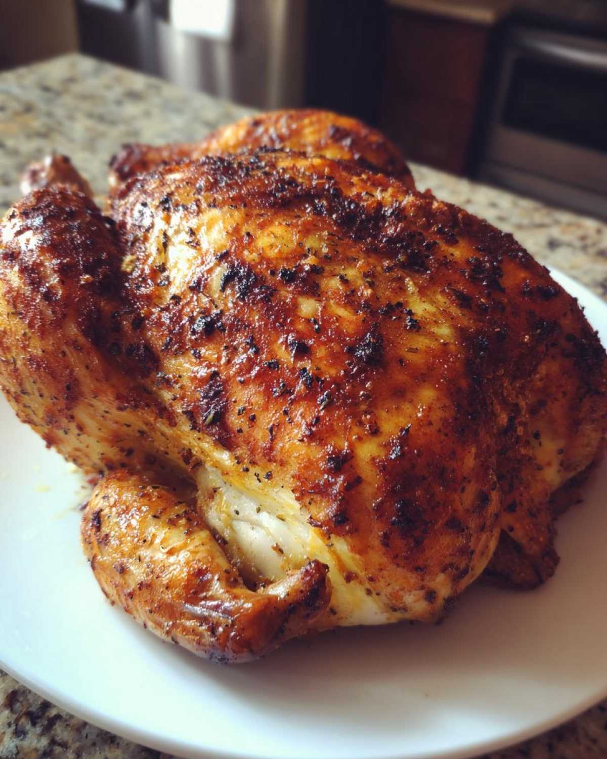 Close-up of a perfectly cooked, crispy-skinned air fryer whole chicken resting on a white plate.