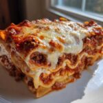 A thick, cheesy slice of amazing 1-dish lasagna with rich meat sauce layers on a white plate.