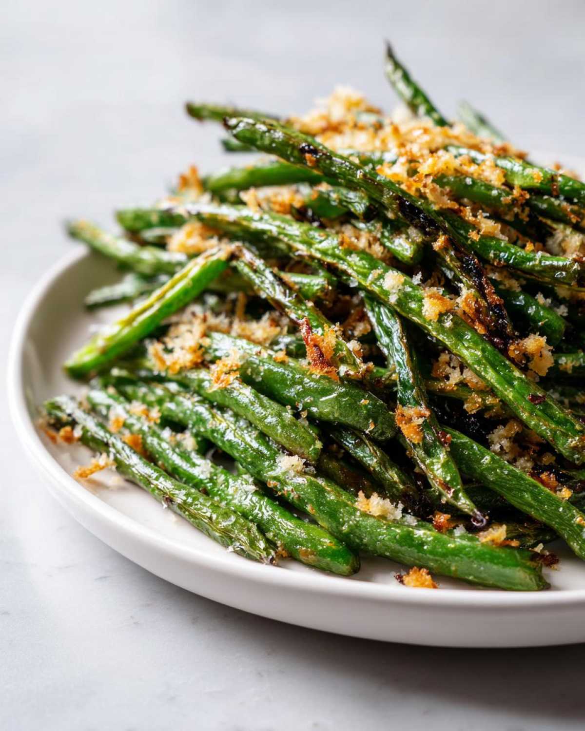Close-up of roasted green beans topped with toasted breadcrumbs served on a white platter.