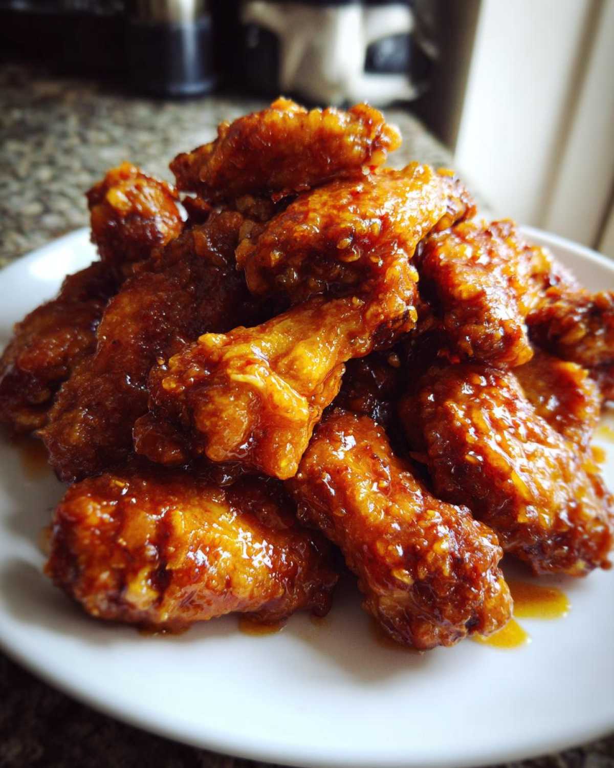 A close-up shot of a mound of perfectly cooked, glossy, glazed chicken wings piled high on a white plate.