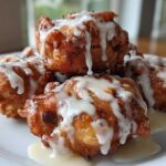 A stack of golden brown, deep-fried apple fritter pieces drizzled generously with white vanilla glaze.