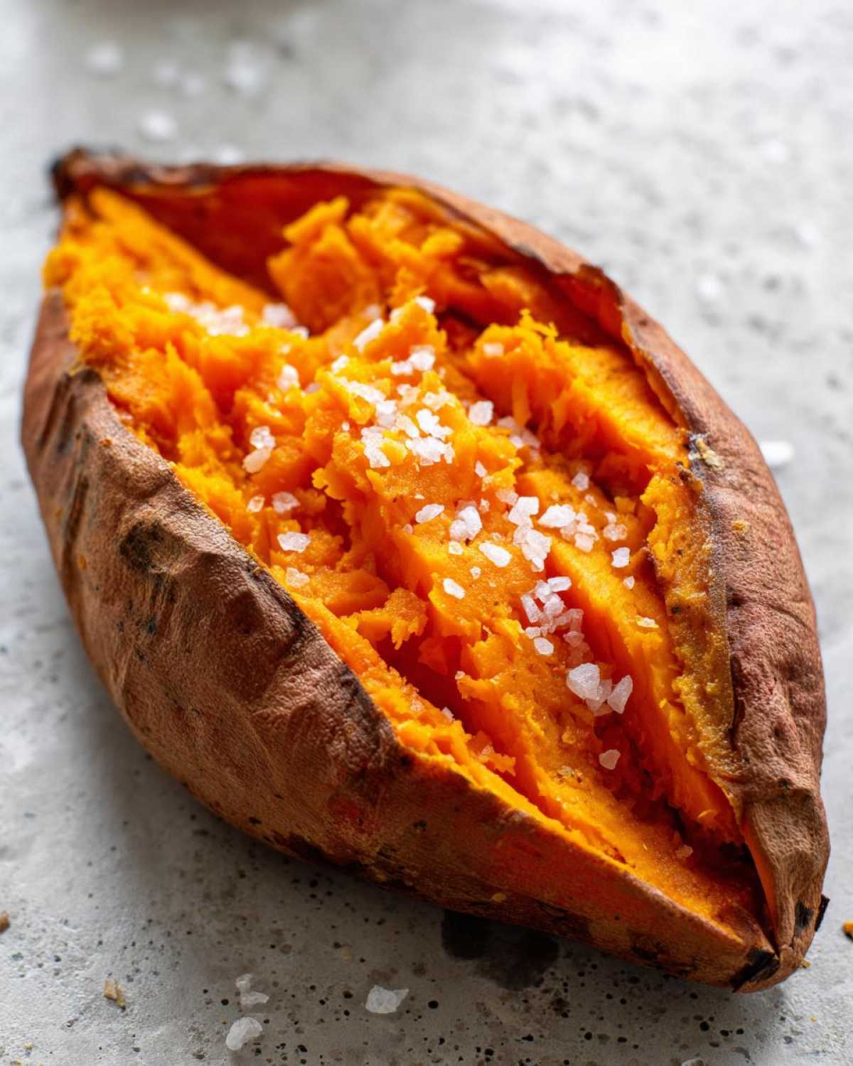 Close-up of a perfectly baked sweet potatoes, split open to show fluffy orange flesh topped with coarse sea salt.