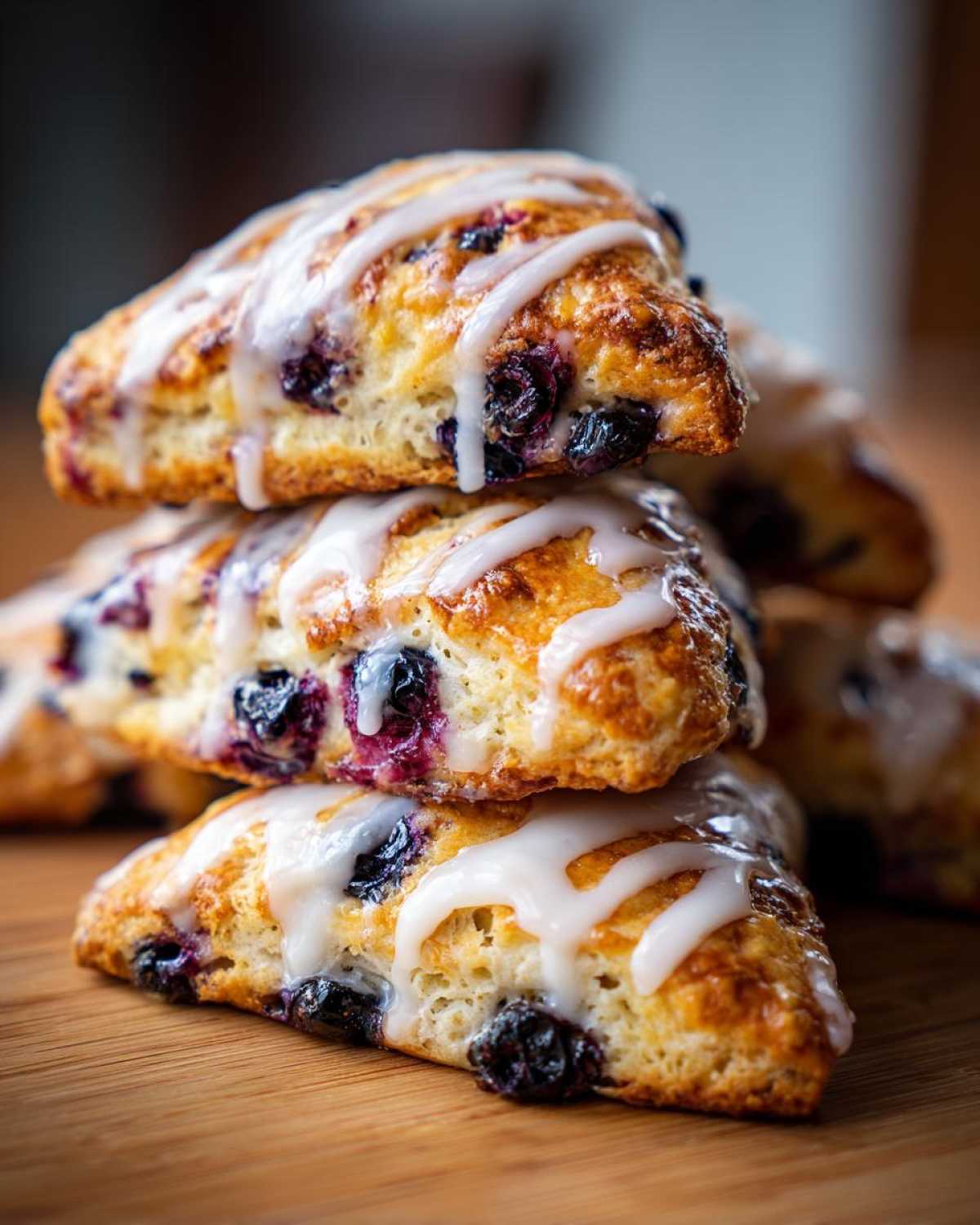 A close-up stack of three fluffy blueberry scones drizzled with white vanilla glaze.