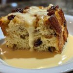 A close-up of a serving of amazing bread pudding topped with raisins and drenched in vanilla cream sauce.