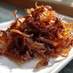 A close-up of a mound of rich, dark brown caramelized onions piled high on a white square plate.