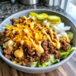 A close-up of a delicious cheeseburger bowl featuring seasoned ground beef, shredded cheddar cheese, special sauce, lettuce, onions, and pickles.
