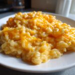 A close-up of a serving of creamy, cheesy rice topped with melted orange cheddar cheese.