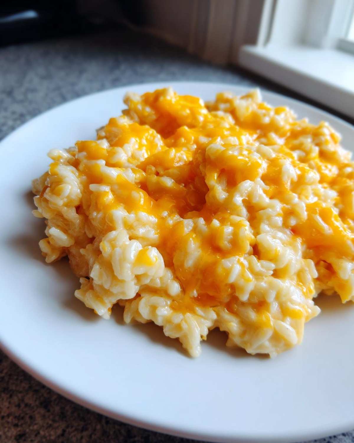 A close-up serving of creamy, delicious cheesy rice topped with melted bright orange cheddar cheese.