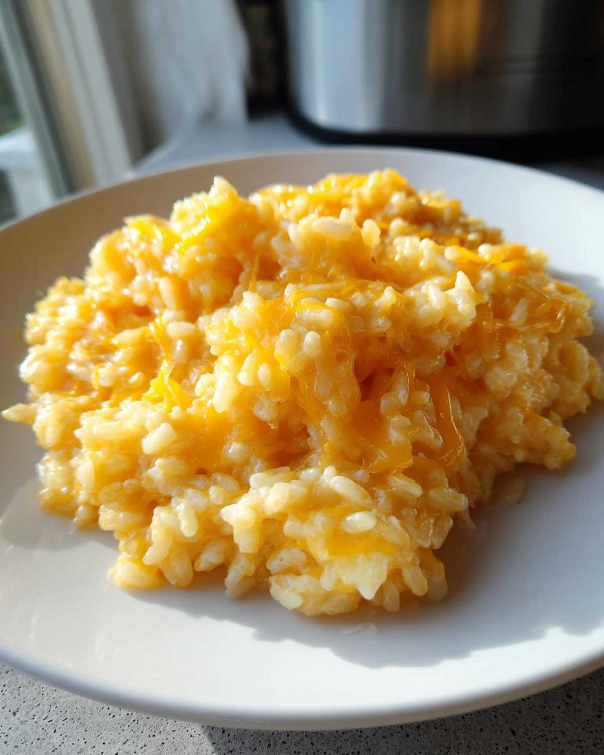 A close-up serving of creamy, white rice topped generously with melted, bright orange cheddar cheese, showcasing the amazing cheesy rice.