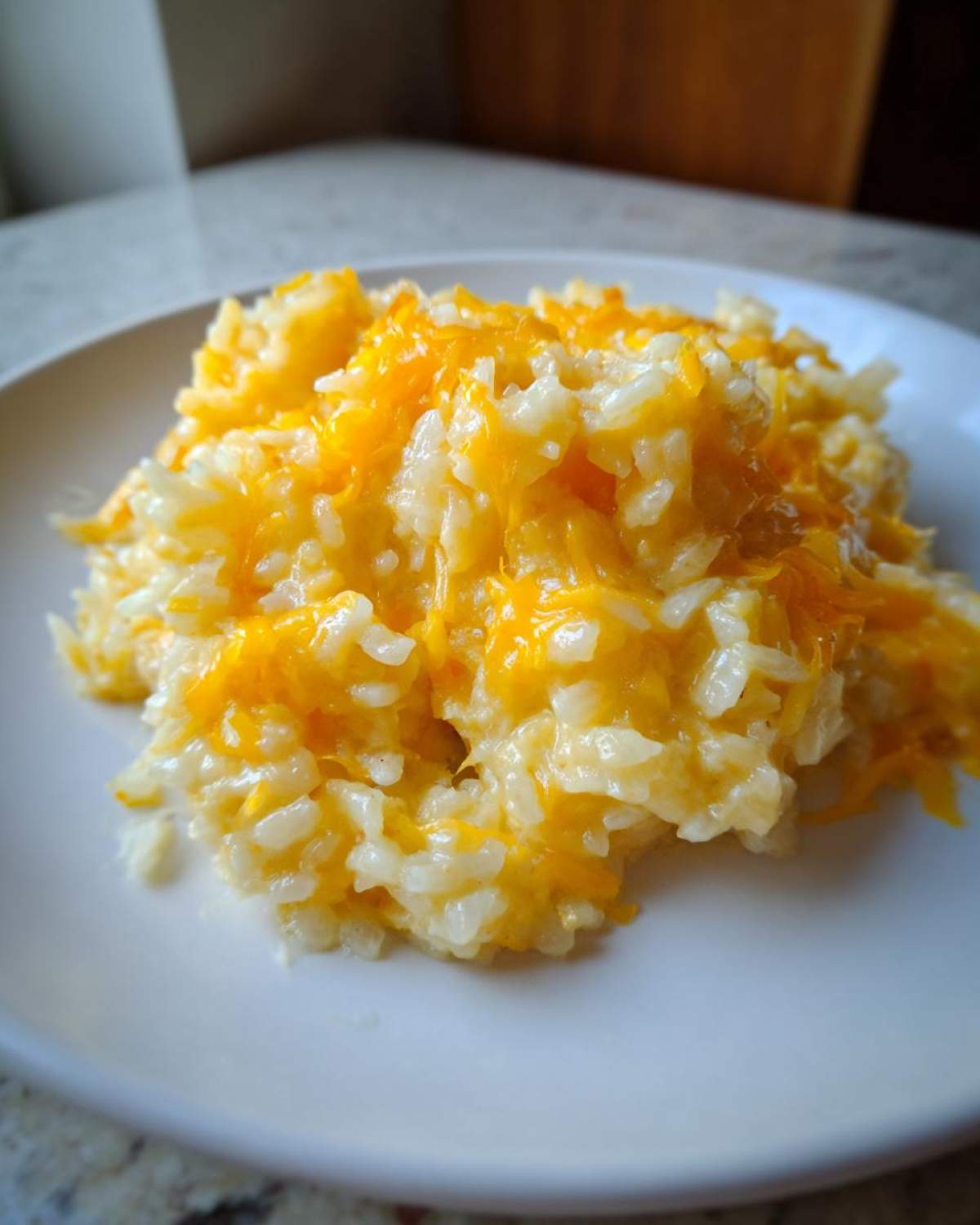 Close-up of a serving of amazing cheesy rice topped with melted, bright orange cheddar cheese on a white plate.