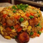 A mound of flavorful chicken fried rice mixed with peas, carrots, and scrambled egg, topped with green onions.