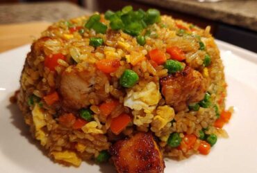 A mound of flavorful chicken fried rice mixed with peas, carrots, and scrambled egg, topped with green onions.