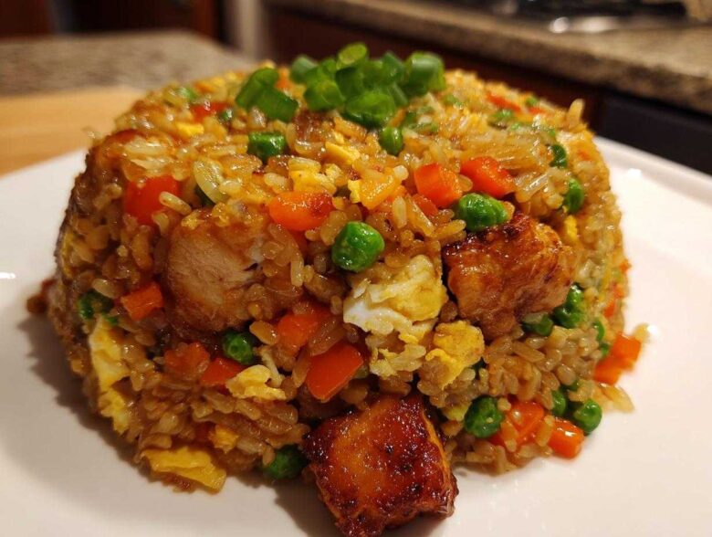 A mound of flavorful chicken fried rice mixed with peas, carrots, and scrambled egg, topped with green onions.