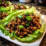 A single serving of savory chicken lettuce wraps filling topped with mushrooms and green onions.