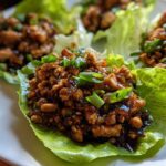 Close-up of saucy ground chicken filling served in crisp lettuce cups for chicken lettuce wraps, garnished with green onions.