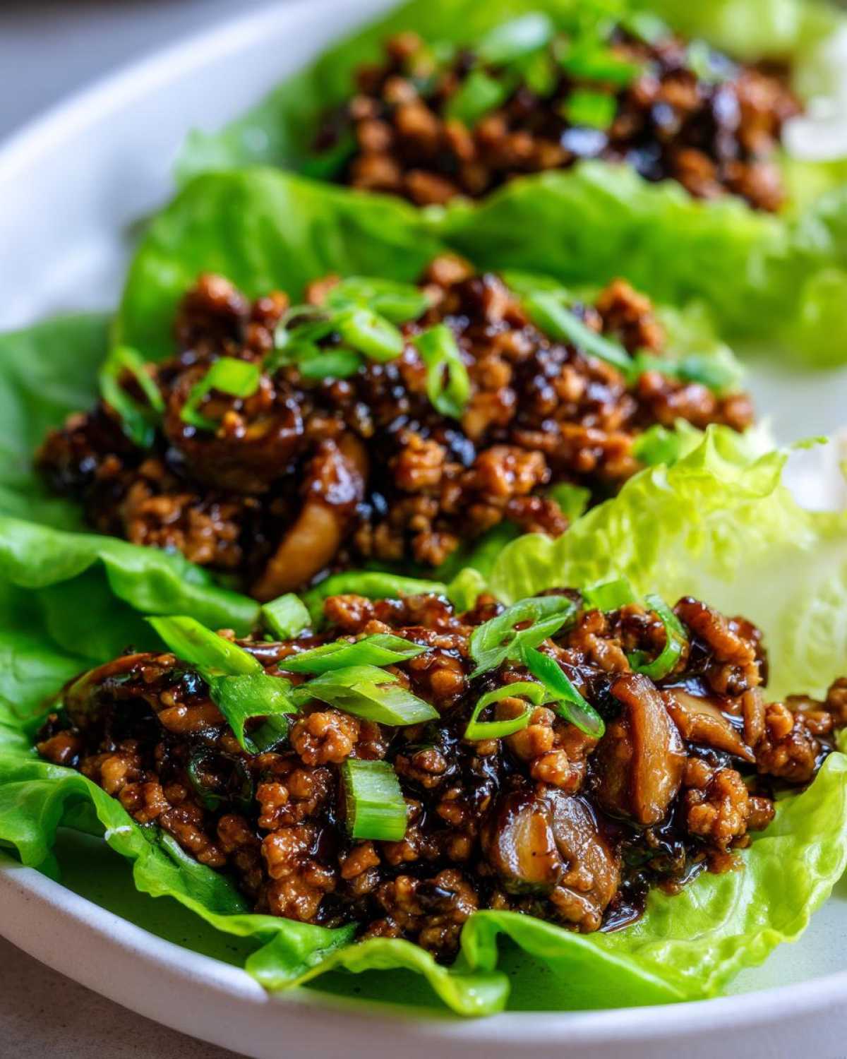 Close-up of three servings of amazing chicken lettuce wraps filled with savory ground chicken mixture and topped with green onions.