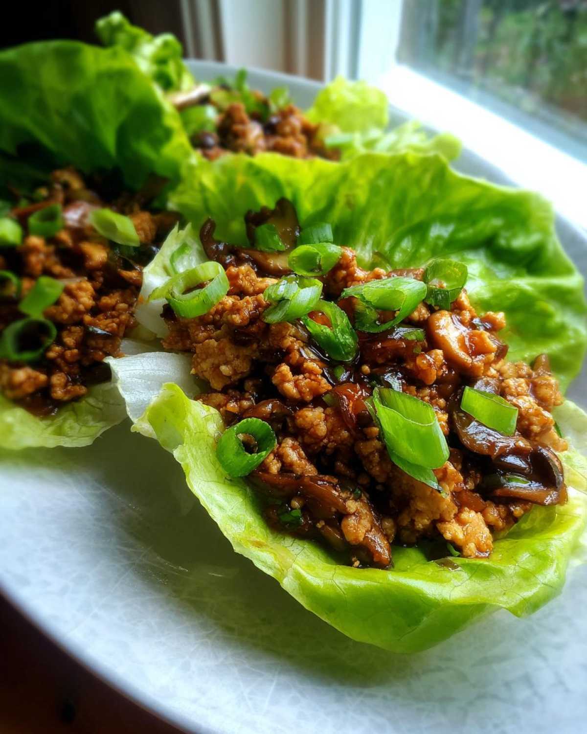 Close-up of flavorful chicken lettuce wraps filled with ground chicken, mushrooms, and topped with fresh green onions.