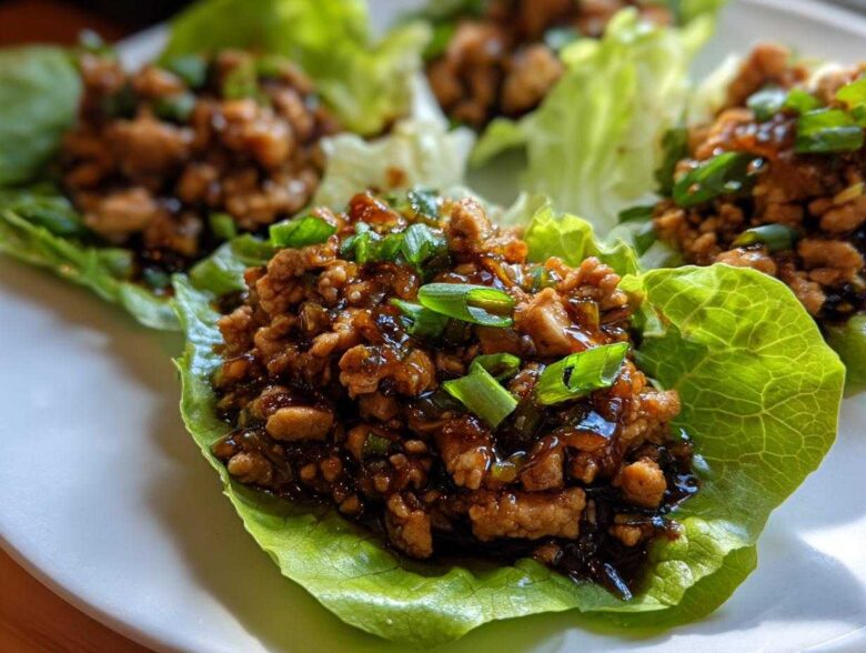 Close-up of saucy ground chicken filling served in crisp lettuce cups for chicken lettuce wraps, garnished with green onions.