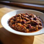 A close-up of a white bowl filled with rich, thick crockpot chili featuring ground beef and kidney beans.