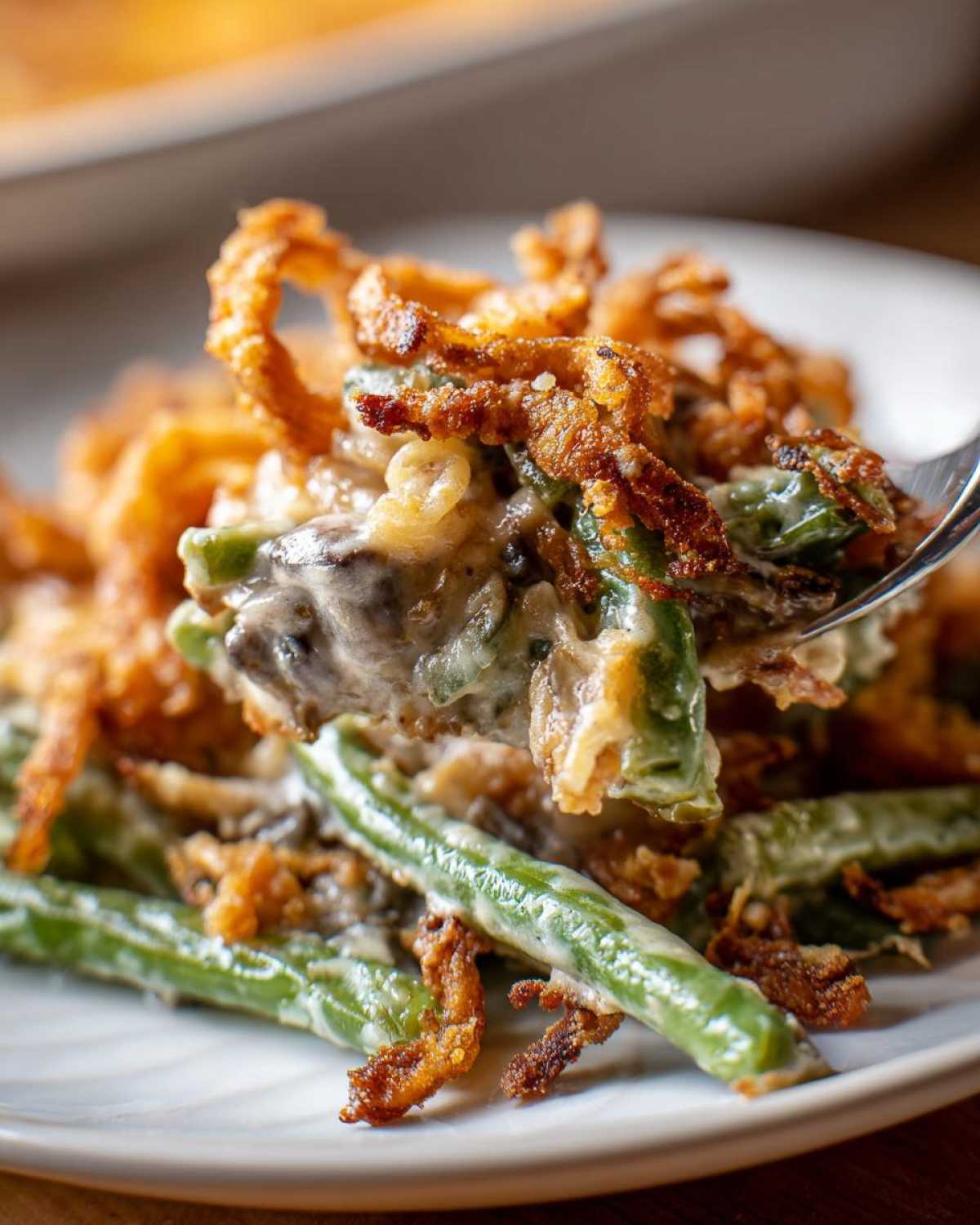A fork lifting a creamy bite of amazing green bean casserole topped with crispy fried onions.