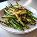 Close-up of bright green beans topped with golden, crispy breadcrumbs.