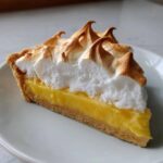 A perfect slice of lemon meringue pie showing thick yellow curd and toasted meringue peaks.