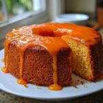A slice cut from a bundt-style orange juice cake topped with a thick, dripping orange glaze.