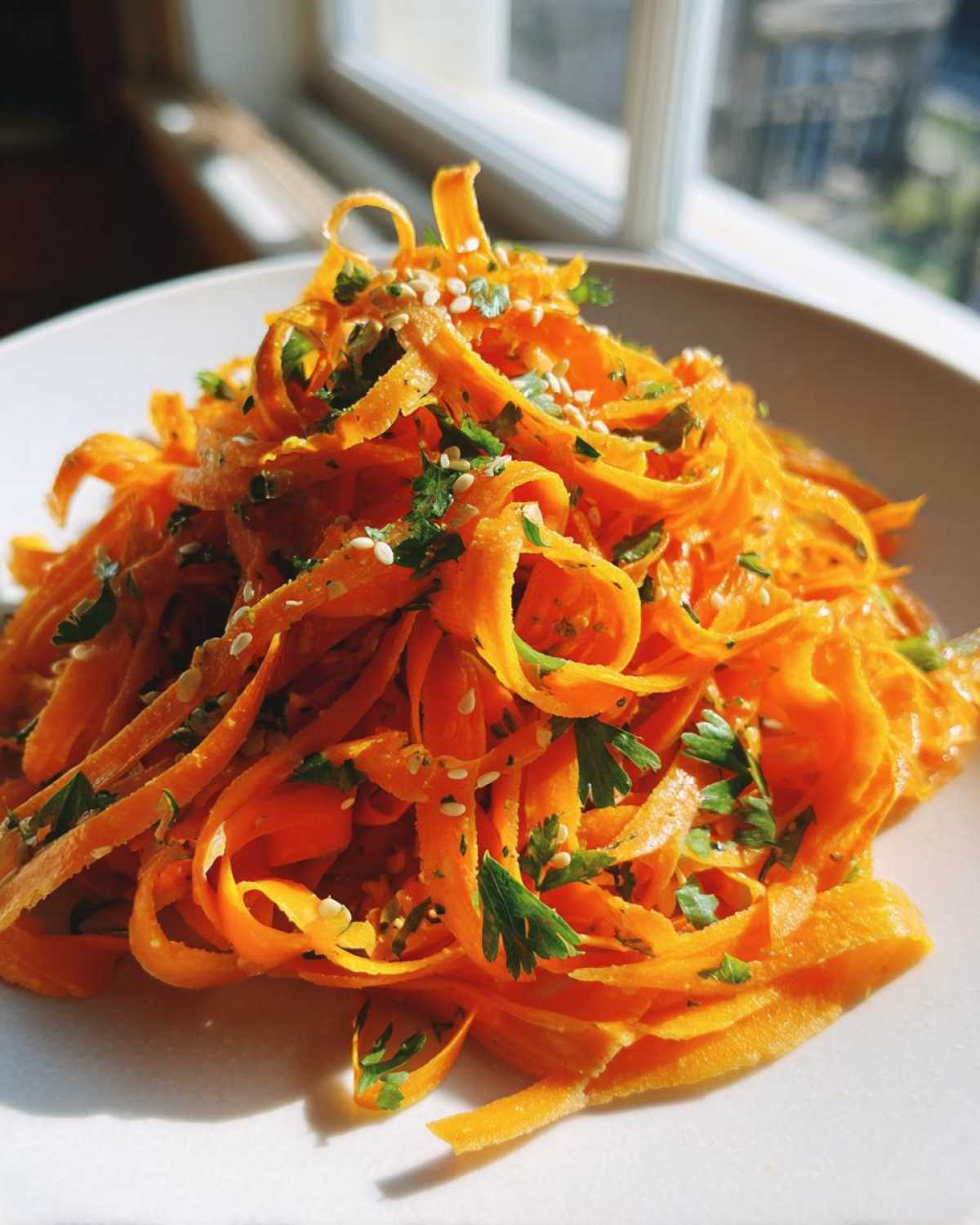 Close-up of vibrant orange raw carrot salad ribbons topped with fresh parsley and sesame seeds.