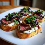 Four pieces of steak crostini featuring medium-rare steak, creamy cheese, and caramelized red onions garnished with parsley.