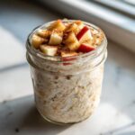 Close-up of apple cinnamon overnight oats in a mason jar, topped with diced red apples and cinnamon.