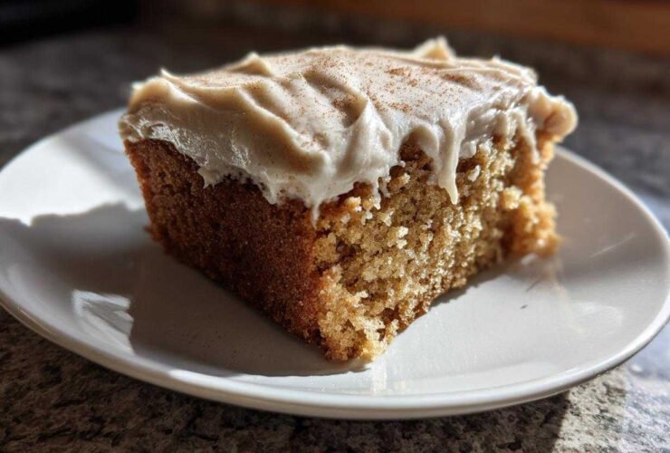 A close-up of a moist slice of applesauce cake topped with creamy frosting and a sprinkle of cinnamon.