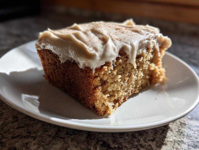 A close-up of a moist slice of applesauce cake topped with creamy frosting and a sprinkle of cinnamon.