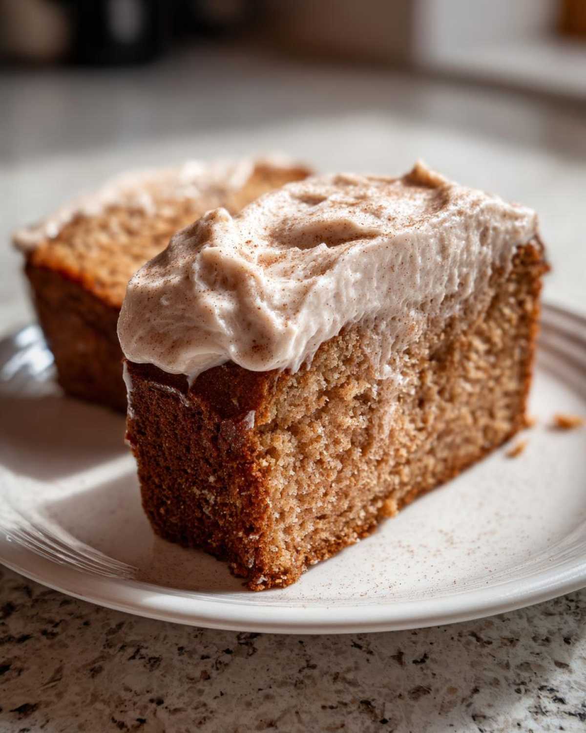 Close-up of a moist slice of applesauce cake topped with thick, cinnamon-dusted frosting.