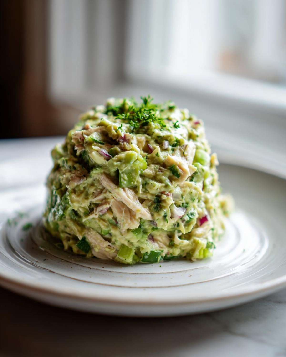 A molded serving of creamy avocado chicken salad topped with fresh parsley on a white plate.
