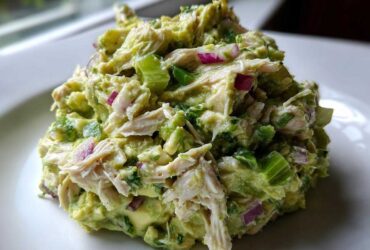 Close-up of a mound of creamy avocado chicken salad featuring shredded chicken, diced red onion, and celery.