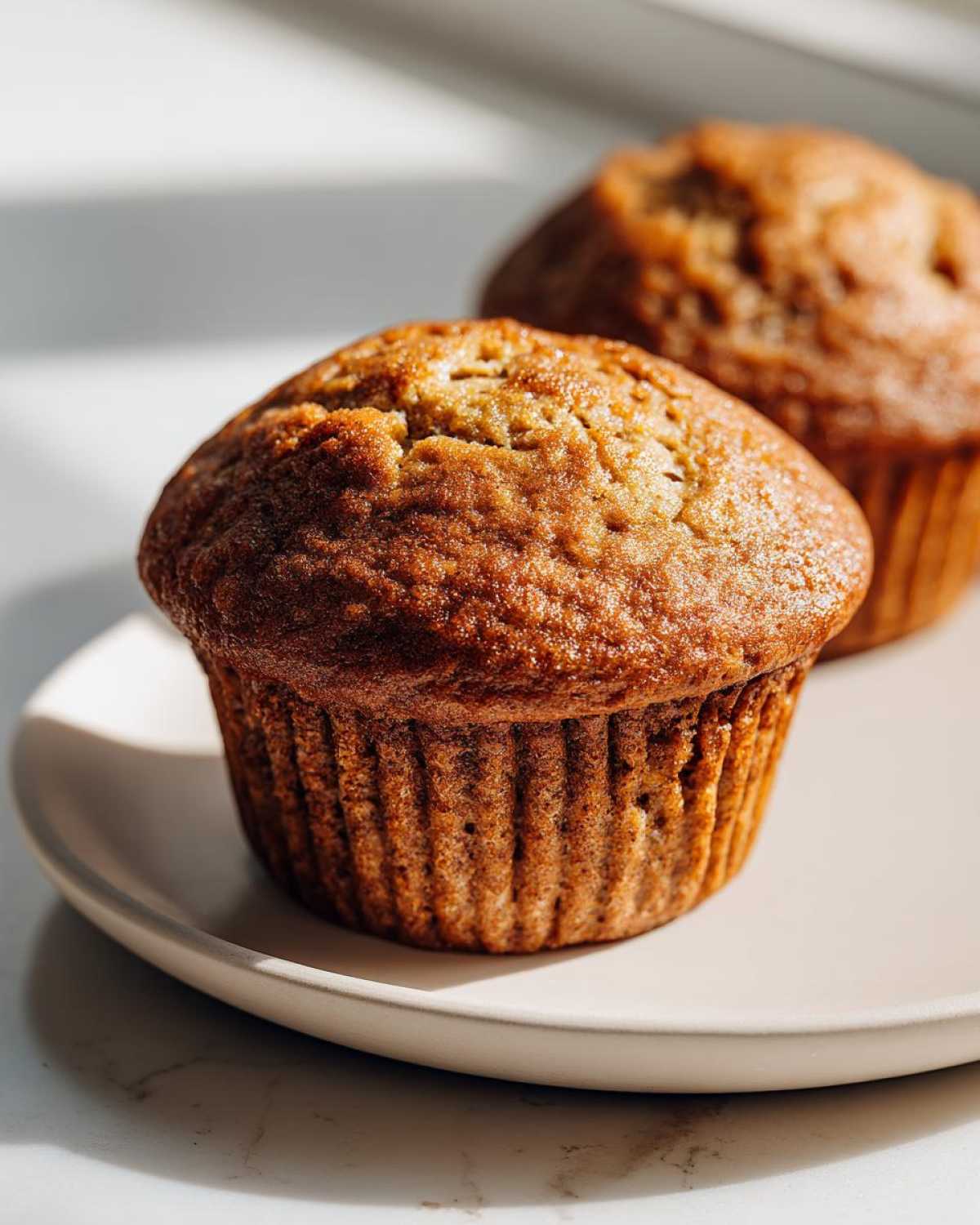 Close-up of two golden brown banana protein muffins sitting on a light-colored plate.