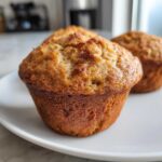 Close-up of a perfectly baked banana protein muffins with a golden brown, domed top resting on a white plate.