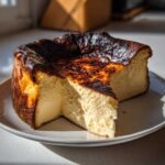A creamy Basque burnt cheesecake with a deeply caramelized, dark top, sitting on a white plate with one slice removed.