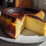 A whole Basque burnt cheesecake with a slice cut out, showcasing its creamy interior and dark caramelized top.