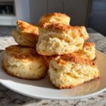 A close-up stack of freshly baked, fluffy scones with golden tops sitting on a white plate.