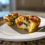 Close-up of a savory egg bite with spinach and bacon, showing a bite taken out, highlighting the fluffy egg texture.