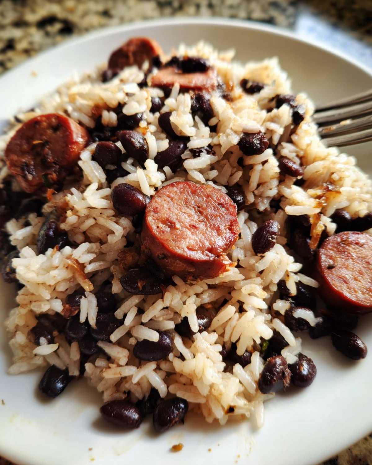 Close-up of a plate featuring savory black beans and rice mixed with slices of smoked sausage.