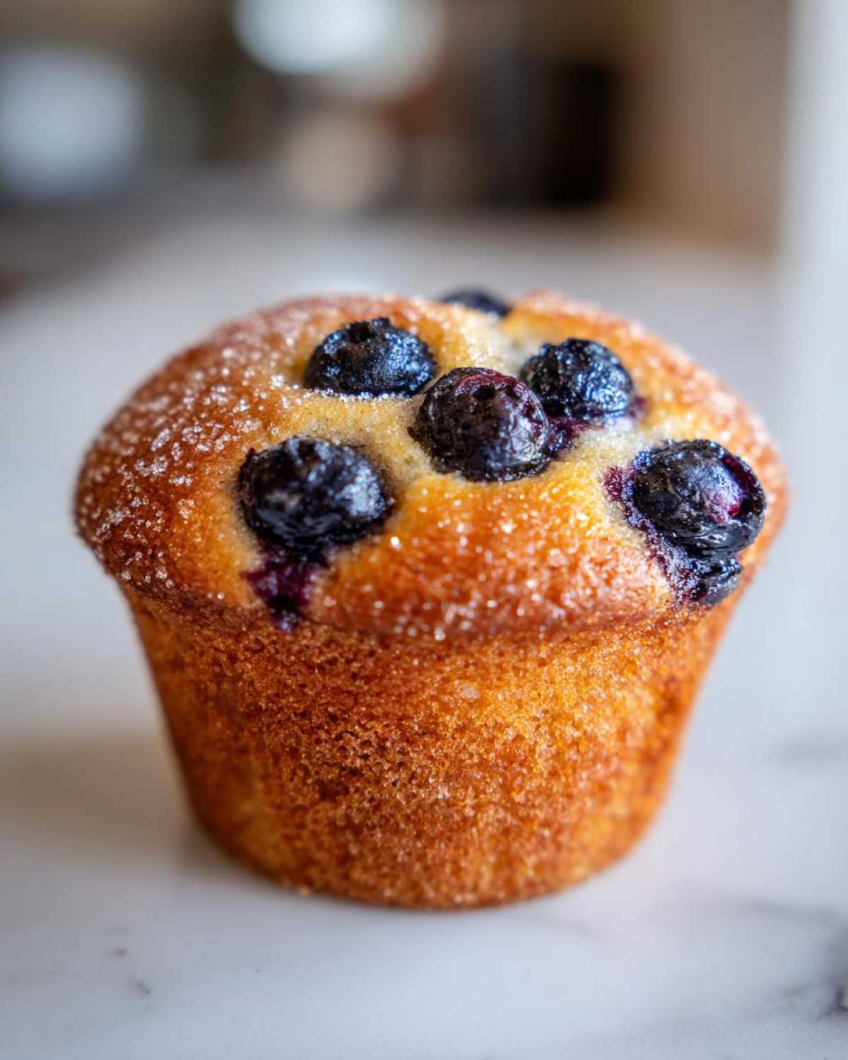 Close-up of a golden-brown blueberry protein muffins topped with coarse sugar crystals.